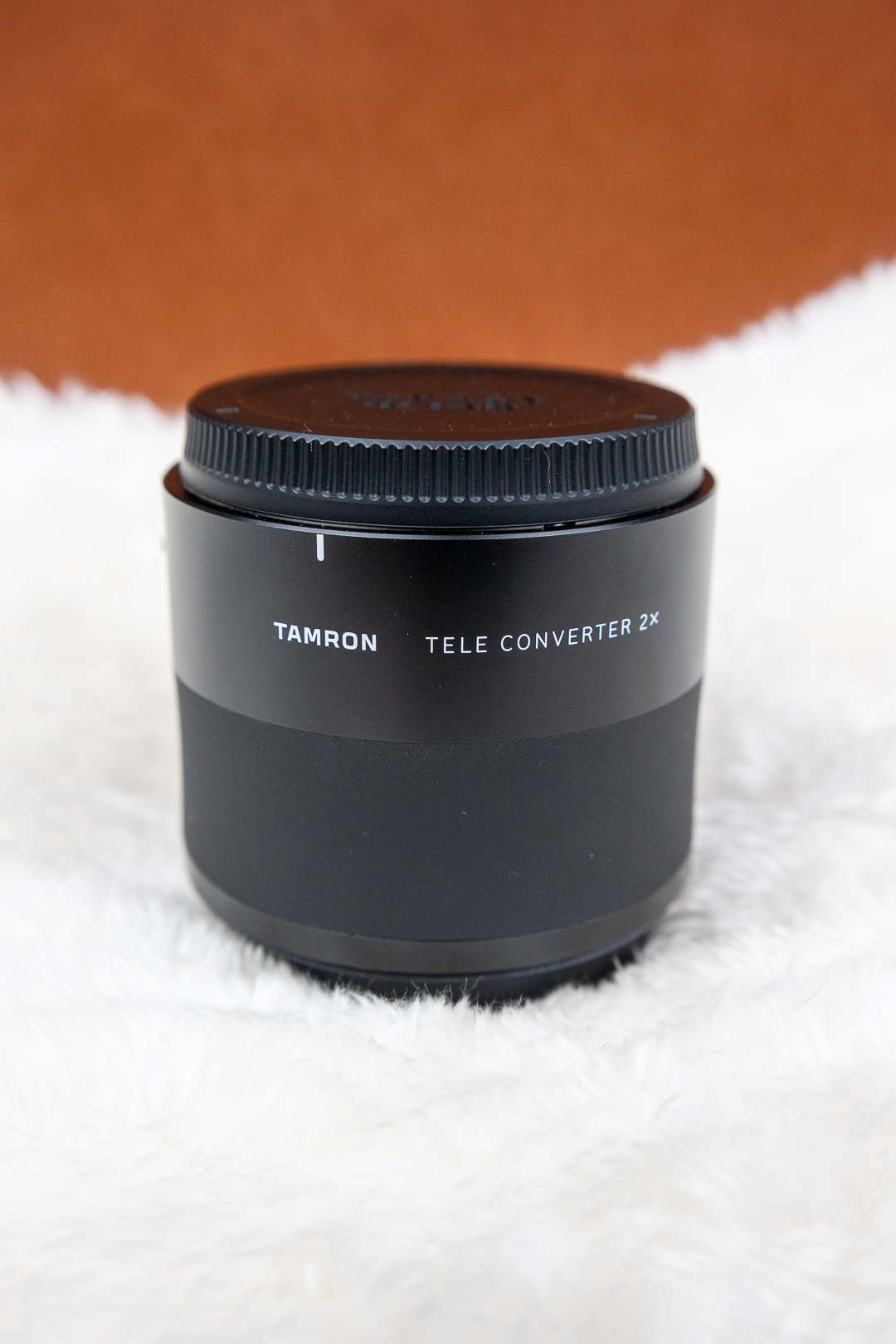 Tamron Teleconverter 2x lens accessory on a black cylindrical body, set on a white fluffy surface.