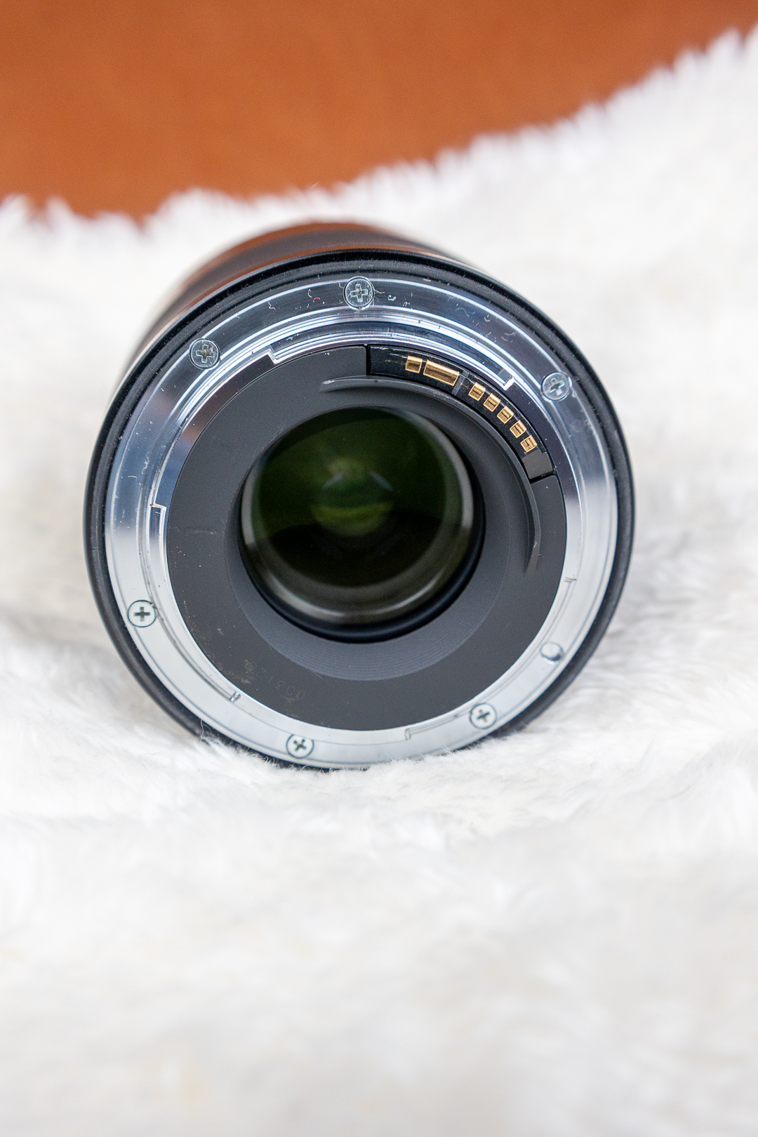 Rear view of a camera lens showing the bayonet mount, gold contact pins, and screws on a chrome ring, resting on white fabric/soft surface.