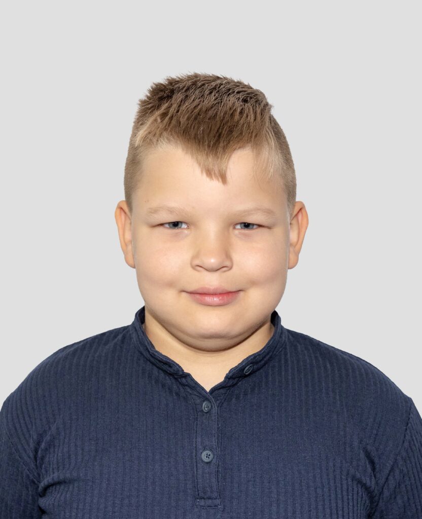 Young boy with short brown hair and a fringe, wearing a navy ribbed shirt against a light grey background.