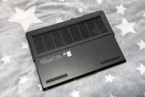 Bottom view of a black laptop with a large vent grille and label, resting on a gray star-pattern blanket.