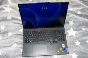 Open Lenovo laptop resting on a gray star-pattern blanket, displaying a blue login screen with 15:45 time.