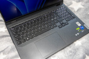 Close-up of a dark grey laptop keyboard on a soft gray patterned surface, with Lenovo/Intel stickers visible on the right.