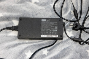 Lenovo laptop power adapter resting on a soft gray blanket with attached cords and plug cables visible.